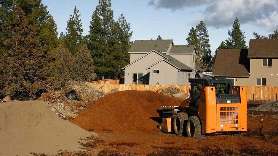An orange skid steer loader moving a pile of brown mulch in a residential yard during a landscaping project