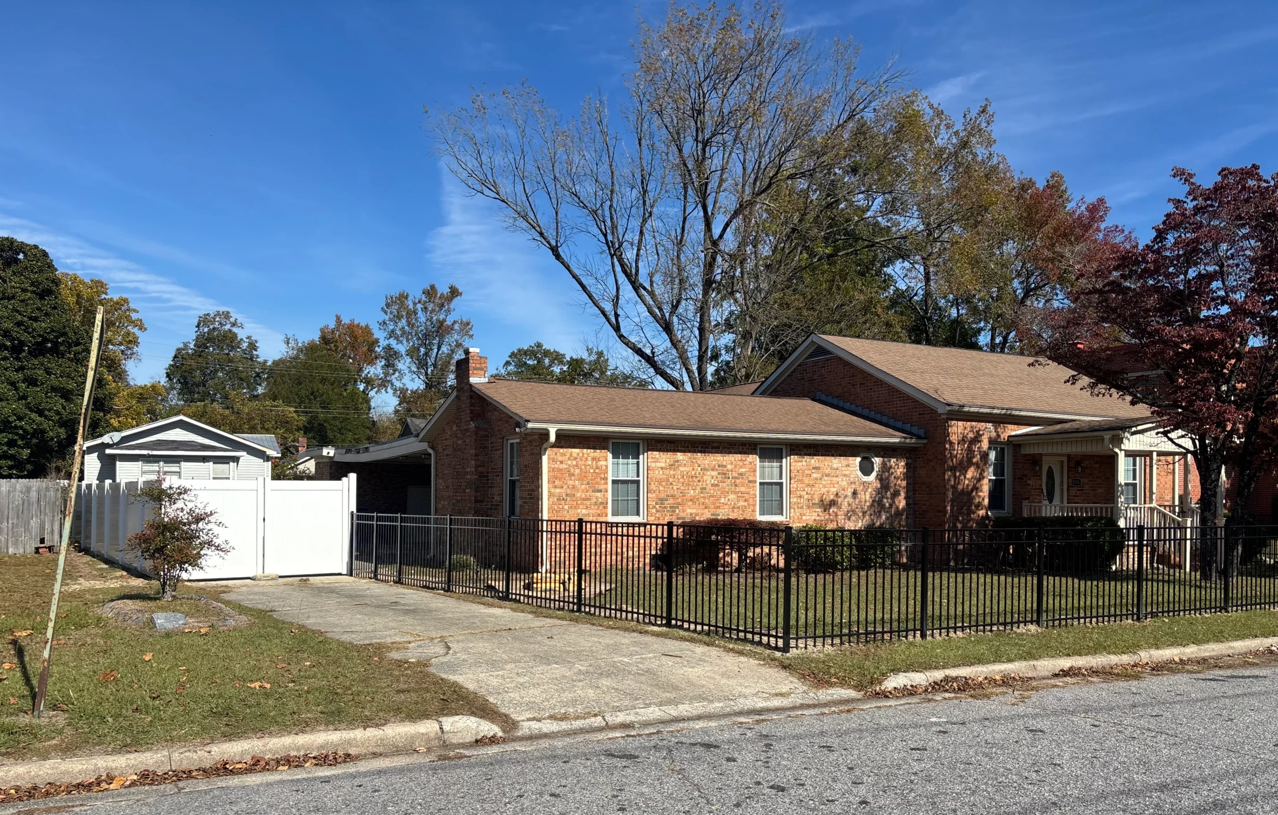 Brick house with a black metal picket fence around the front lawn and a white privacy fence by the driveway