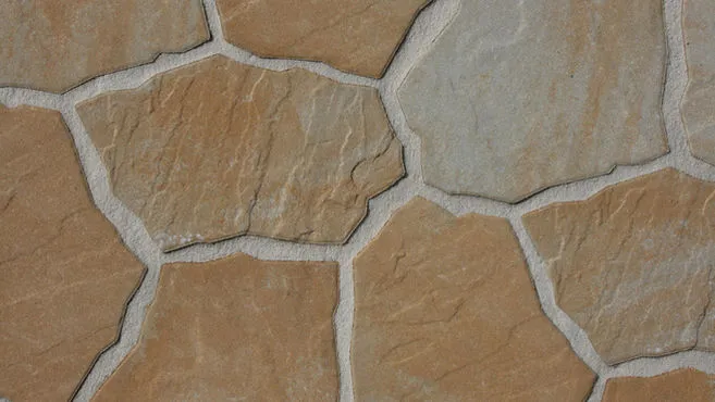 Close-up of flagstone paving with irregular tan and gray stones joined by light gray mortar